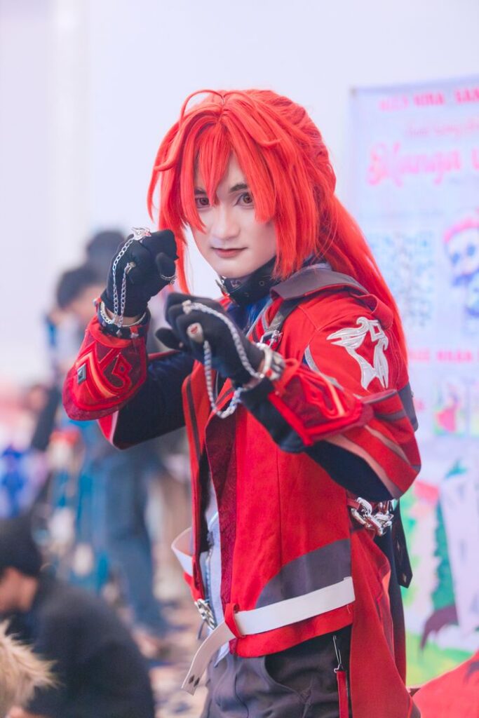 Vibrant cosplay character with red hair and outfit posing at a convention.