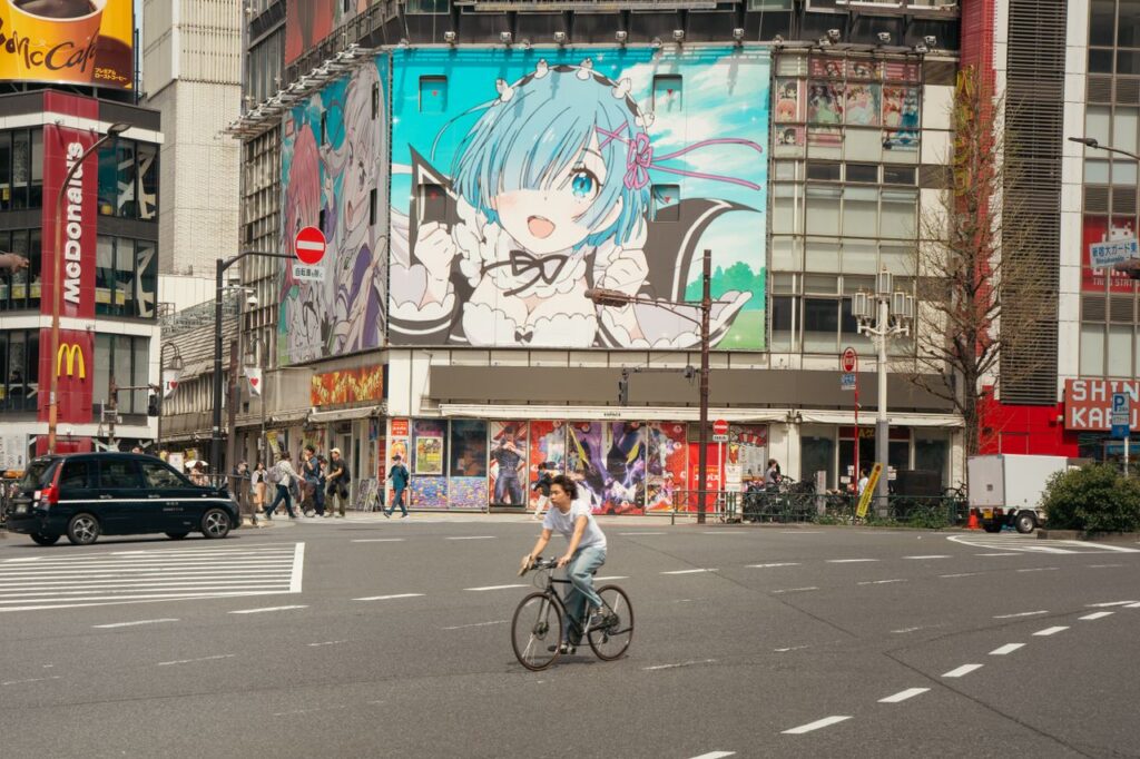 Street scene in Tokyo with anime billboard and cyclist crossing.